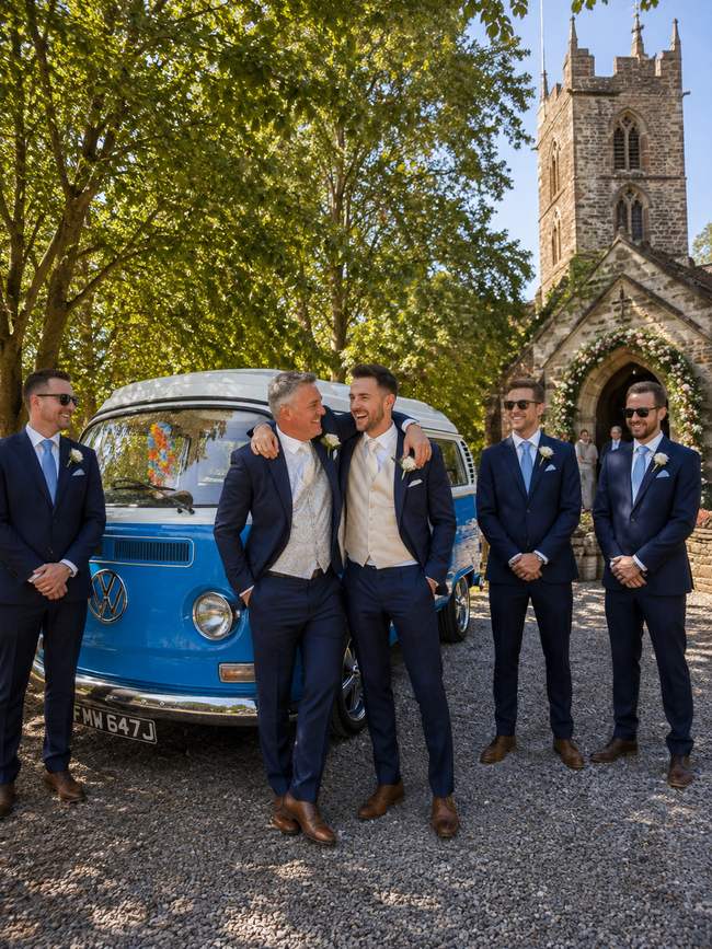 The groomsmen, three deep and grinning, church behind them.